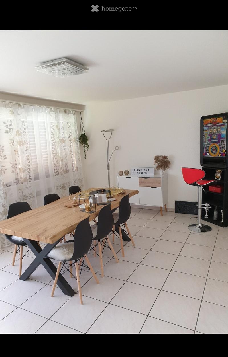 Modern dining room with a wooden dining table, black chairs, a red stool, an arcade machine, a white cabinet, and a floor lamp.
