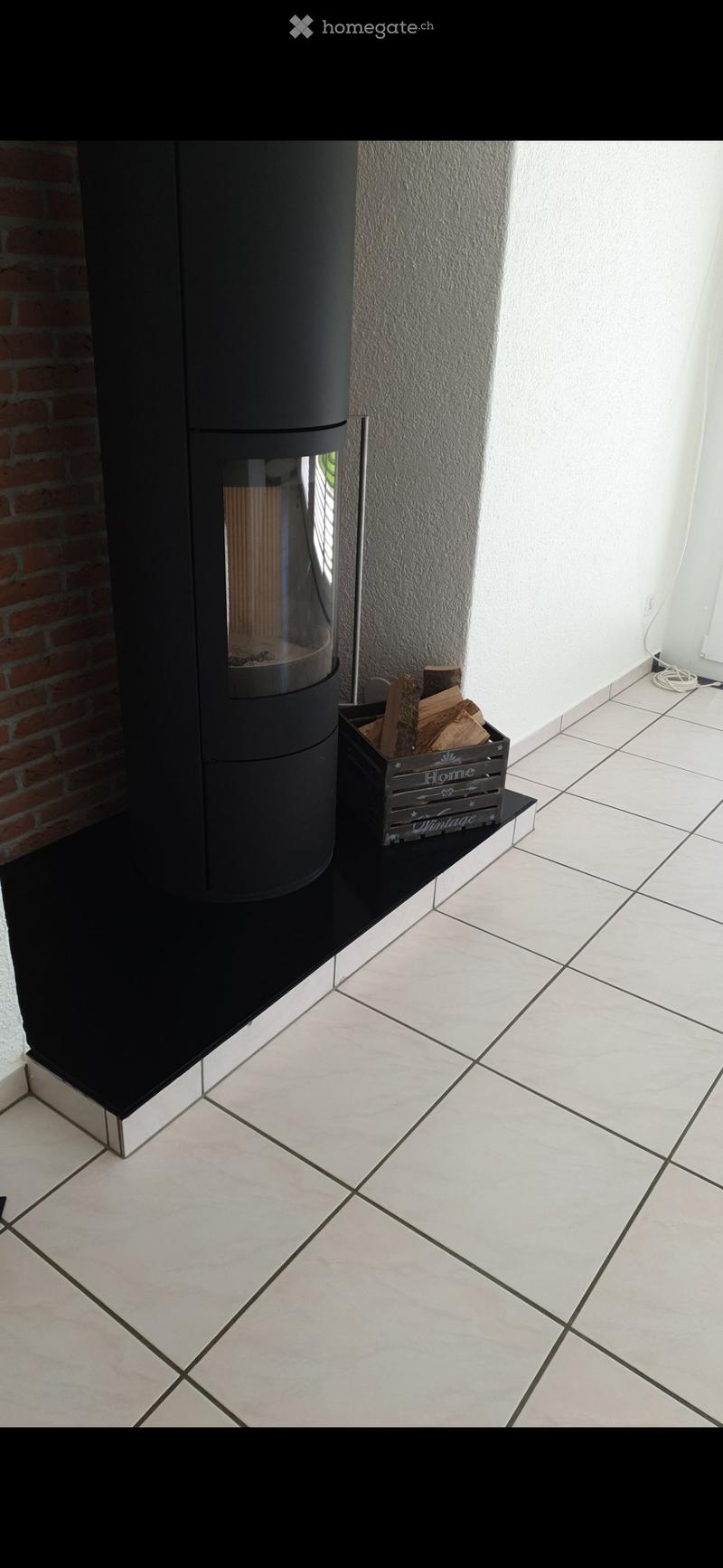 Modern fireplace with a sleek black design, accompanied by a wooden crate holding logs, set against a textured wall and tiled floor.