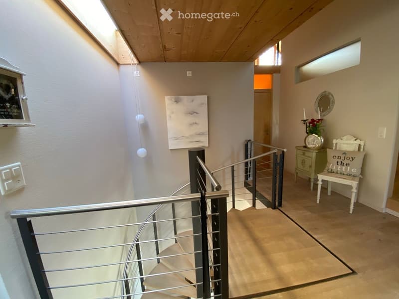 Spacious hallway with modern staircase, wooden ceiling, and contemporary decor including artwork and a small seating area.