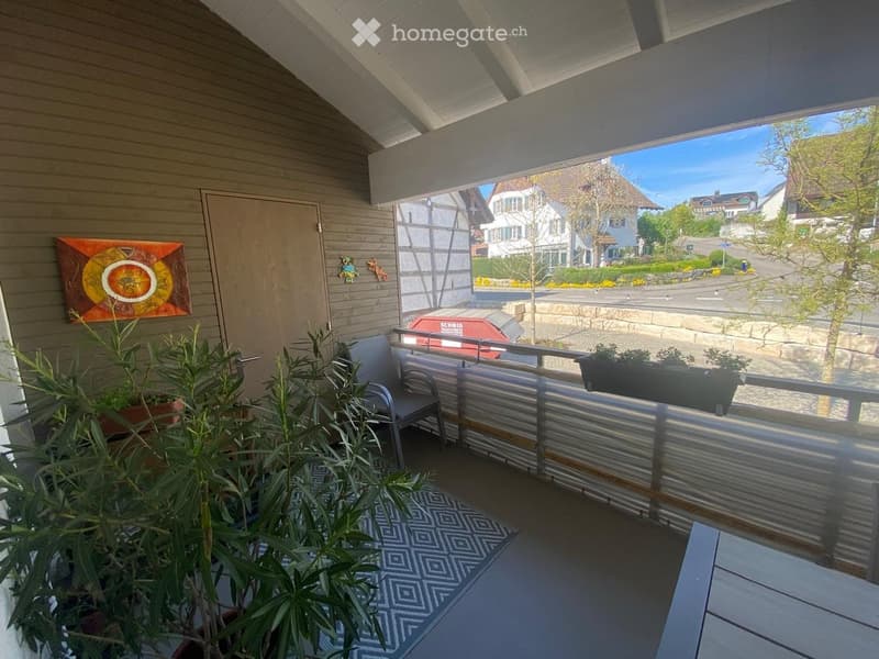 Balcony with a chair, potted plants, and a view of a residential street.