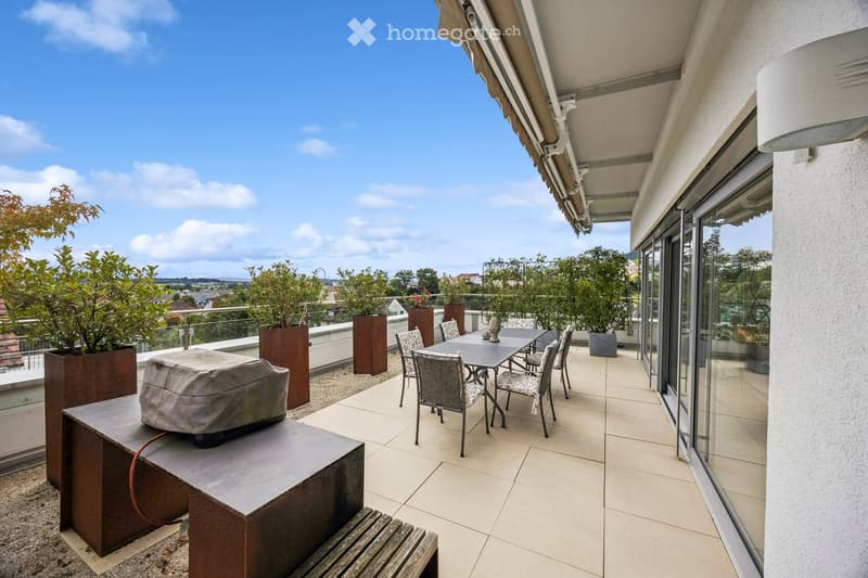 Balcony / Terrace. Balcony with tiled floor, glass railing, outdoor furniture including a table, chairs, and a covered bench, surrounded by potted plants and a scenic view.