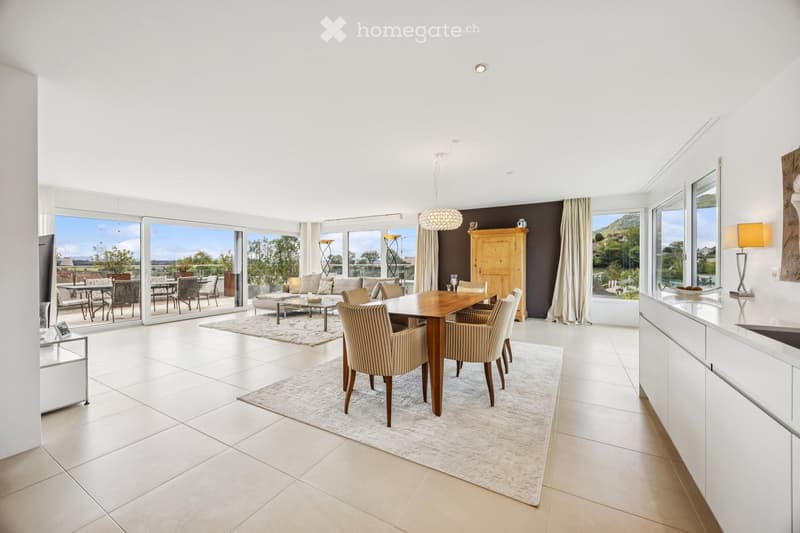 Furnished Room. Bright, open-plan living and dining area with large windows and sliding doors leading to a balcony. Features a dining table with chairs, a sofa with coffee table, a wooden cabinet, and modern lighting.