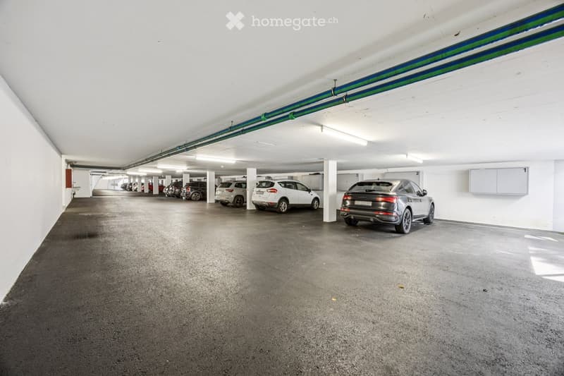 Underground parking area with several parked cars, white walls, concrete floor, and numbered parking spots.