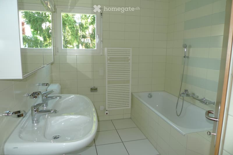 Modern bathroom with a double sink, bathtub, mirror, radiator, and tiled walls and floor.