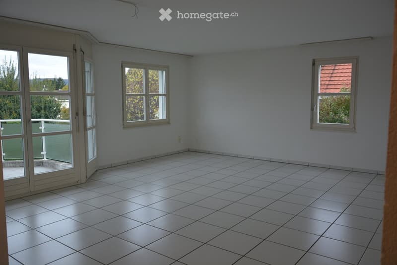 Empty room with white tiled floor, large windows, and a sliding glass door leading to a balcony area.