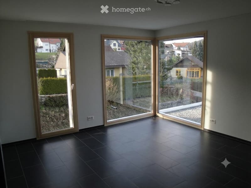 Empty room with dark tiled floor and large sliding glass doors leading to a garden area.