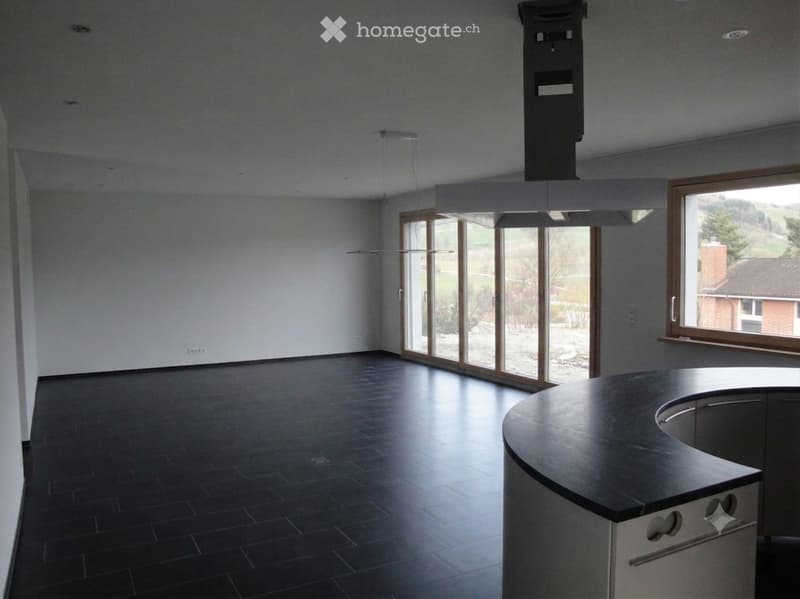 Empty room with dark tiled floor, white walls, large windows, and a kitchen island with sink.