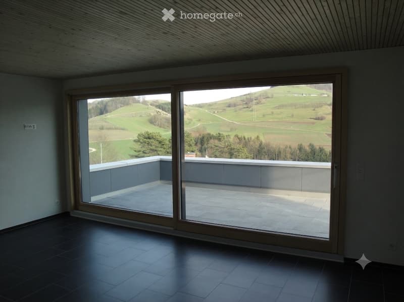 Modern room with large sliding glass doors opening to a balcony, offering scenic countryside views.