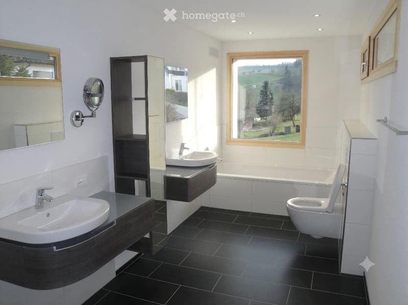 Modern bathroom with black tiled floor, white walls, two sinks, a toilet, a bathtub, and a large window offering a scenic view.