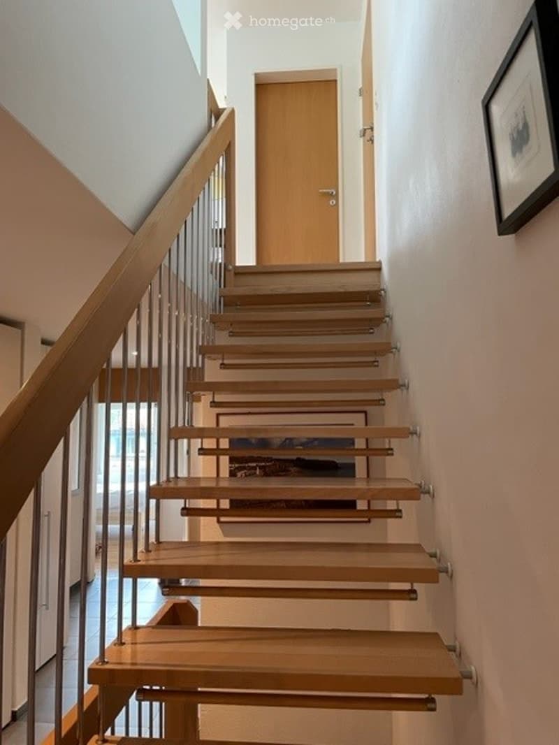 Modern staircase with wooden steps and a metal railing, leading to a closed door at the top.