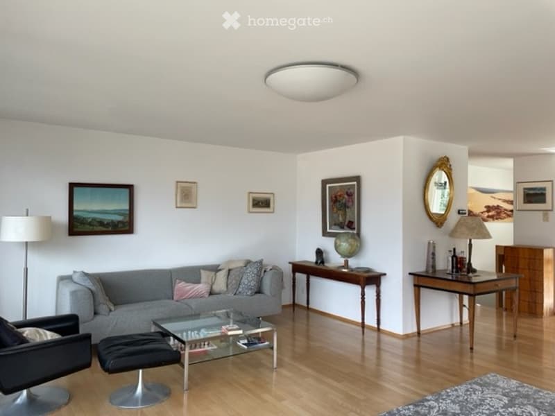 Modern living room with grey sofa, coffee table, ottoman, armchair, side tables, lamps, and artwork on the walls.