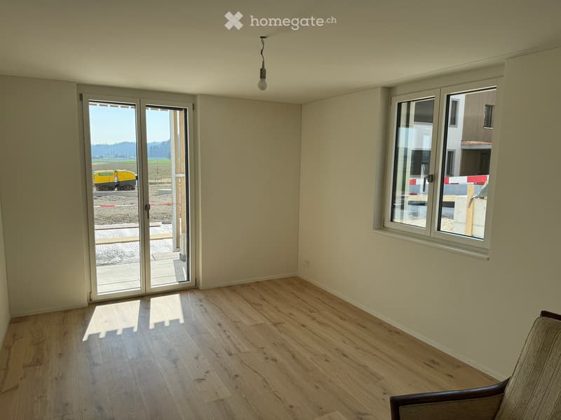 Empty room with light wooden flooring, large sliding glass door leading outside, and a single sofa in the corner.