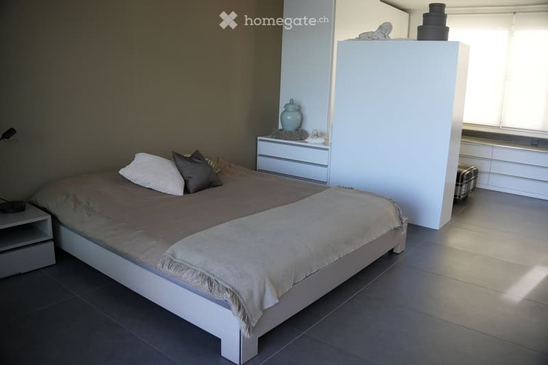 Modern bedroom with a white bed, nightstand, drawer unit, and decorative items including a vase and a stool.