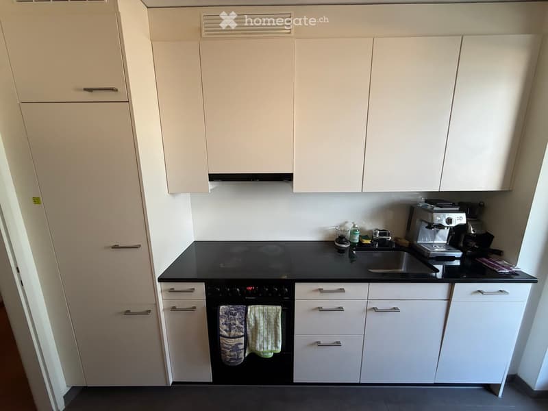 Modern kitchen with white cabinets, black countertop, built-in oven, sink, and coffee maker.