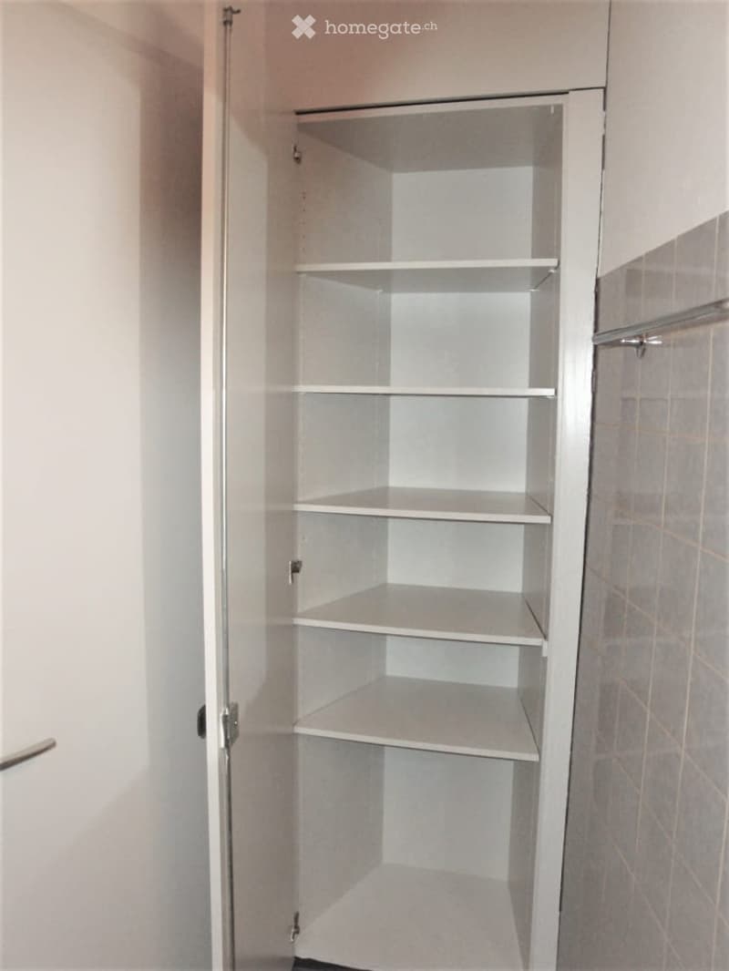 Empty closet with multiple white shelves, located next to a tiled wall and a door frame.