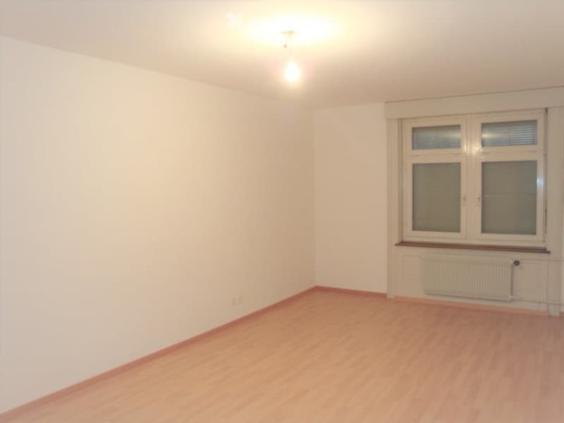 Empty room with wooden flooring, white walls, and large windows with blinds. No furniture or equipment present.