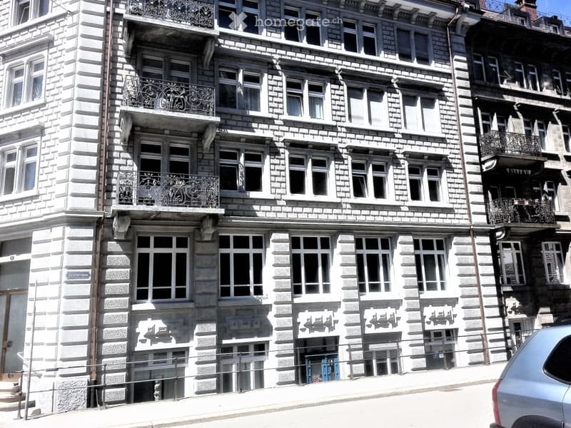 Multi-story building with stone facade, multiple windows, and balconies with ornate railings.