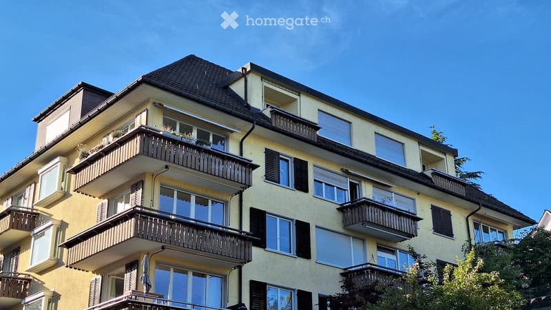 Multi-story residential building with balconies, large windows, and a sloped roof.