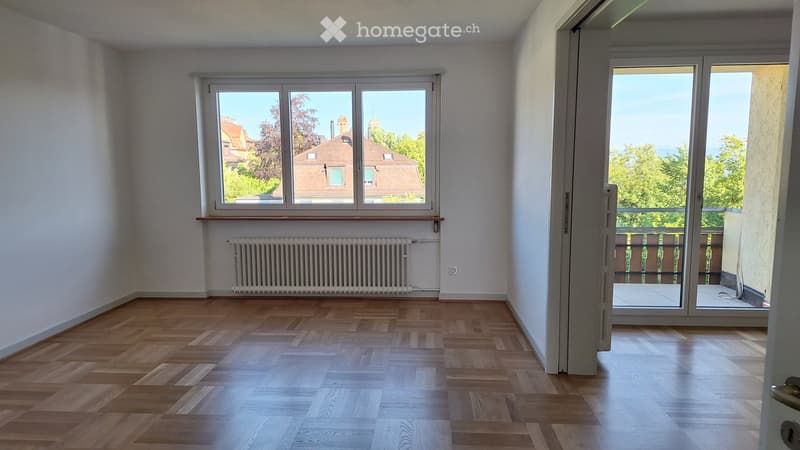 Empty room with wooden flooring, large window, radiator, and sliding glass door leading to a balcony.