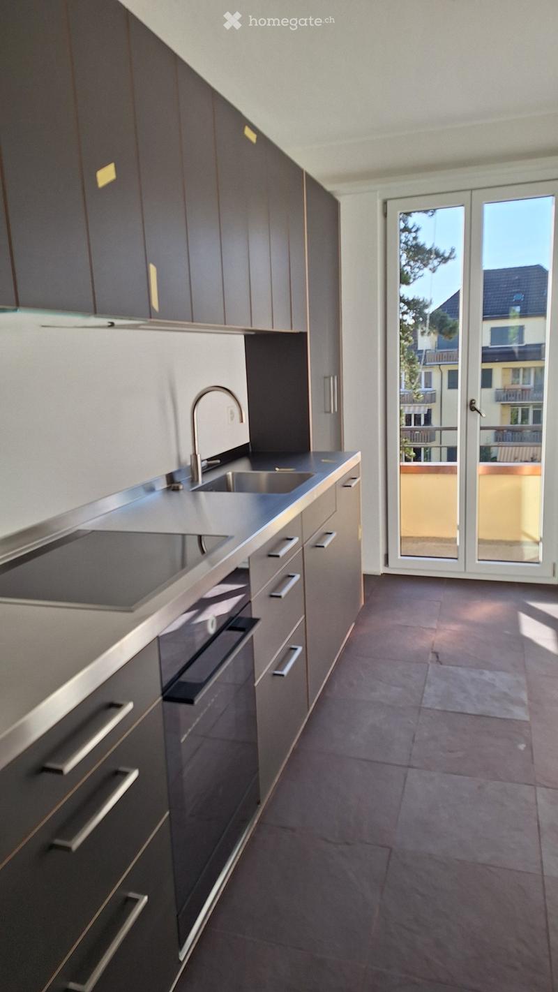 Modern kitchen with dark grey cabinets, stainless steel sink, and a sliding glass door leading to a balcony.