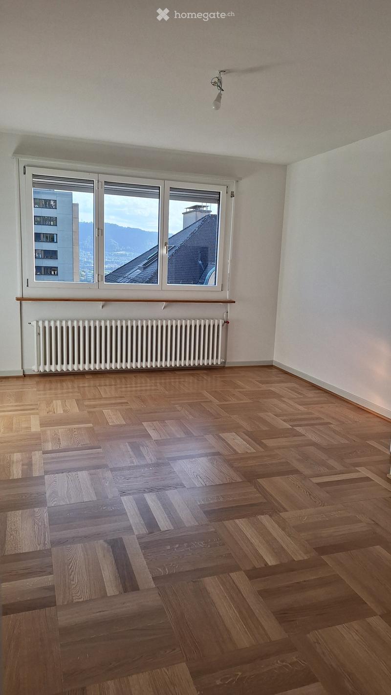 Empty room with wooden flooring, large windows, radiator, and a ceiling light fixture.