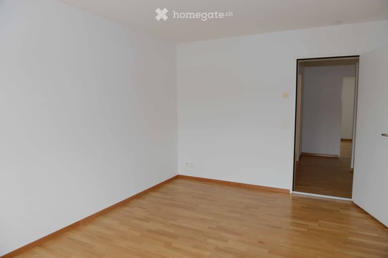Empty room with white walls and wooden flooring, featuring a doorway leading to another room.