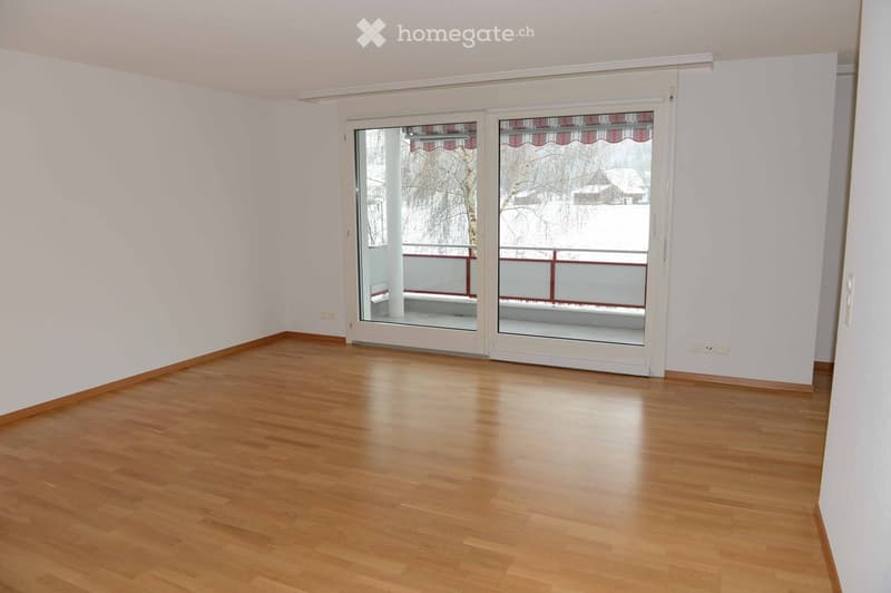 Empty room with light wooden flooring and white walls, featuring large sliding glass doors leading to a balcony with a view of a snowy outdoor area.