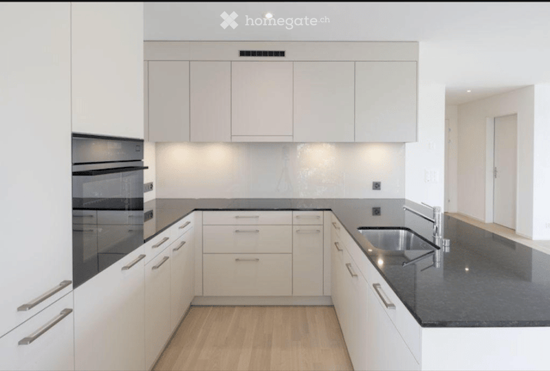 Modern kitchen with white cabinets, black countertops, and stainless steel appliances including an oven and sink.