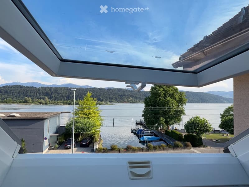 Balcony overlooking a lake with boats, trees, and distant mountains.