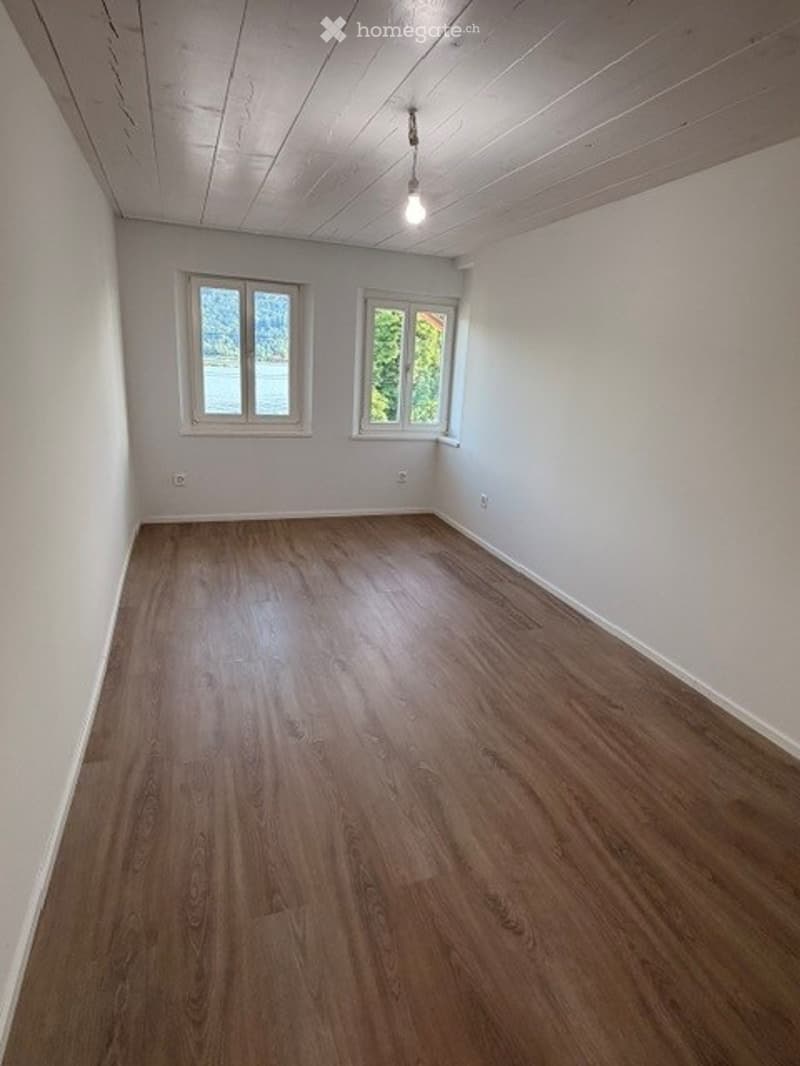 Empty room with wooden flooring, white walls, and two windows letting in natural light. No furniture or equipment present.