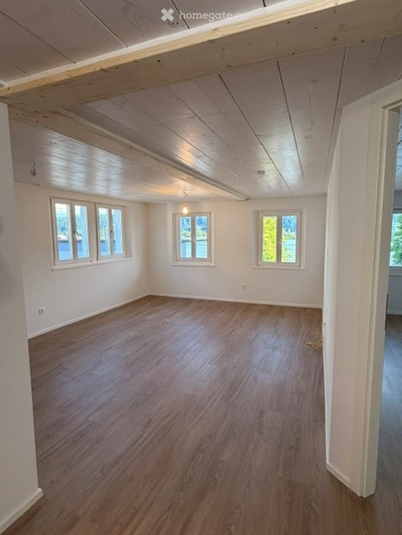 Empty room with wooden flooring, white walls, and large windows offering a view of the water.