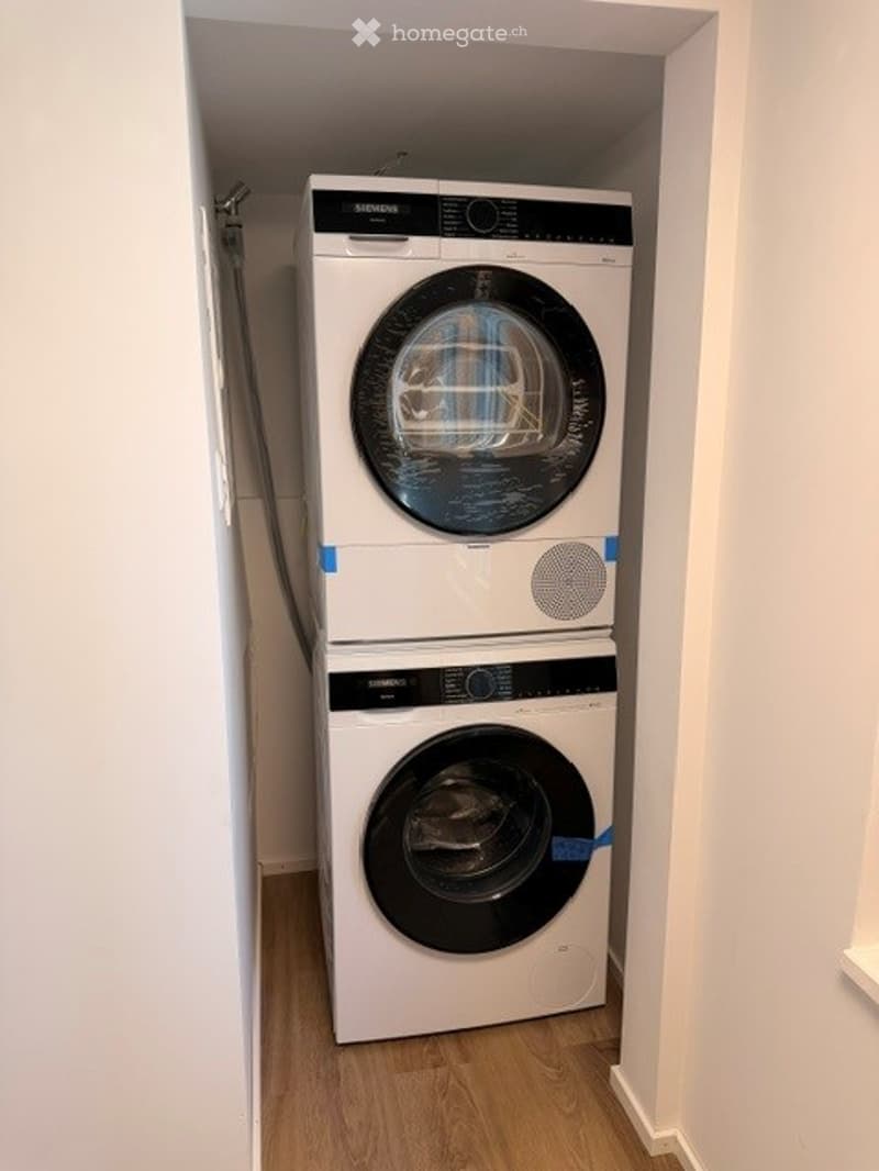 Compact bathroom with a stacked washing machine and dryer unit, white walls, and light wooden flooring.