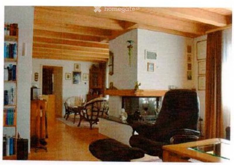 Cozy living room with wooden ceiling beams, fireplace, sofa, chair, small table, and bookshelf.