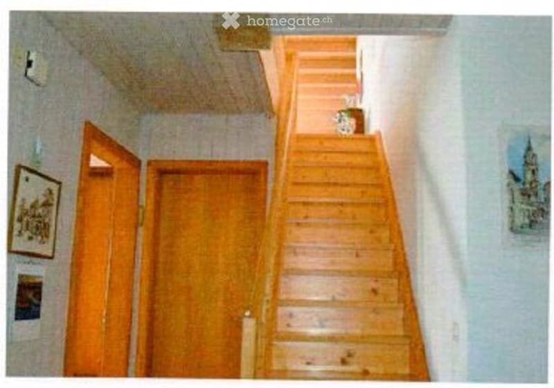 Wooden staircase leading up, open wooden door on left, closed wooden door on right, framed pictures on walls.