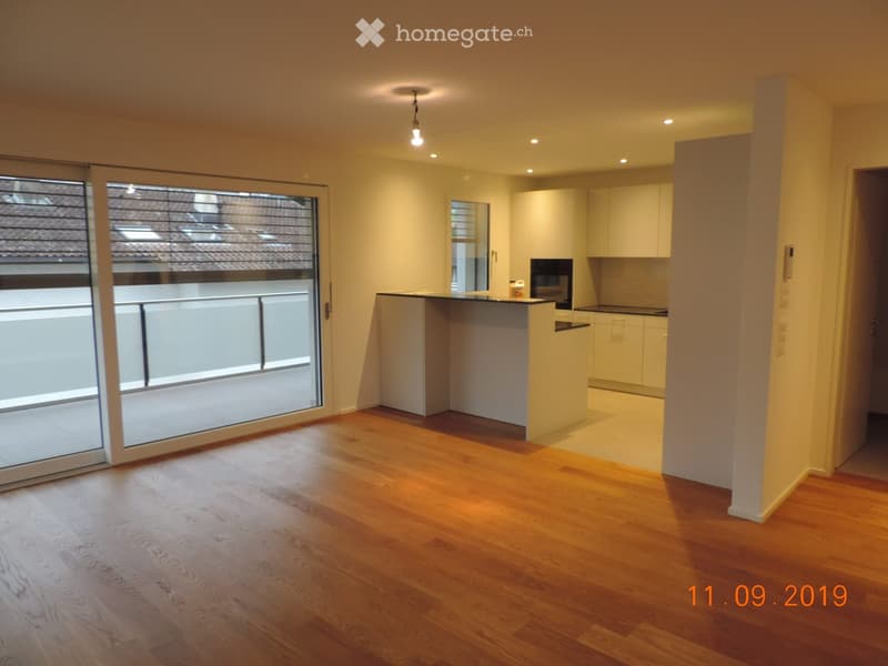 Open-plan living and dining area with wooden flooring, white kitchen cabinets, and a large sliding glass door leading to a balcony.