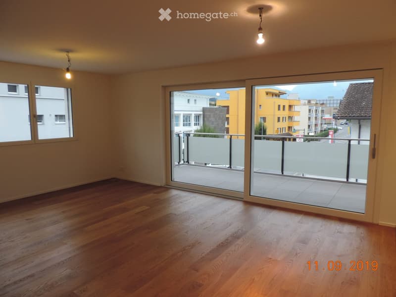 Empty room with wooden flooring, large sliding glass doors leading to a balcony, and natural light from windows.