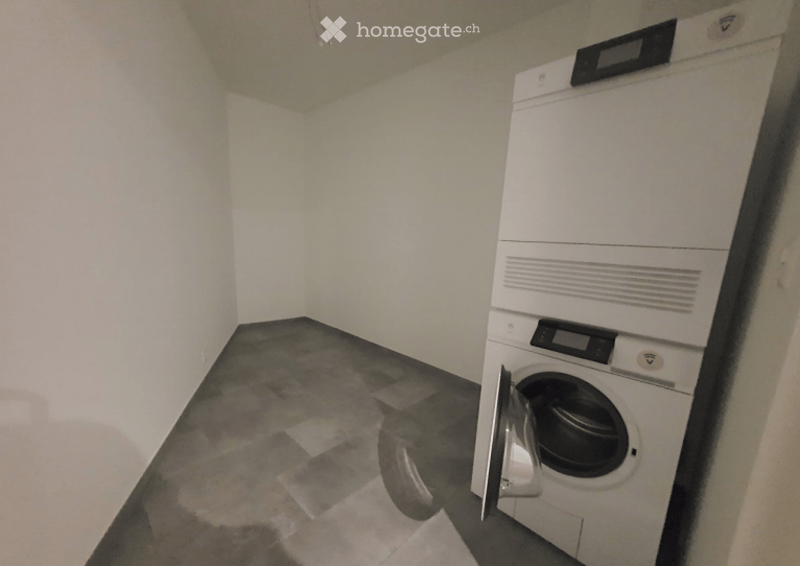 A small, unfurnished room with a washing machine, tiled floor, and white walls.