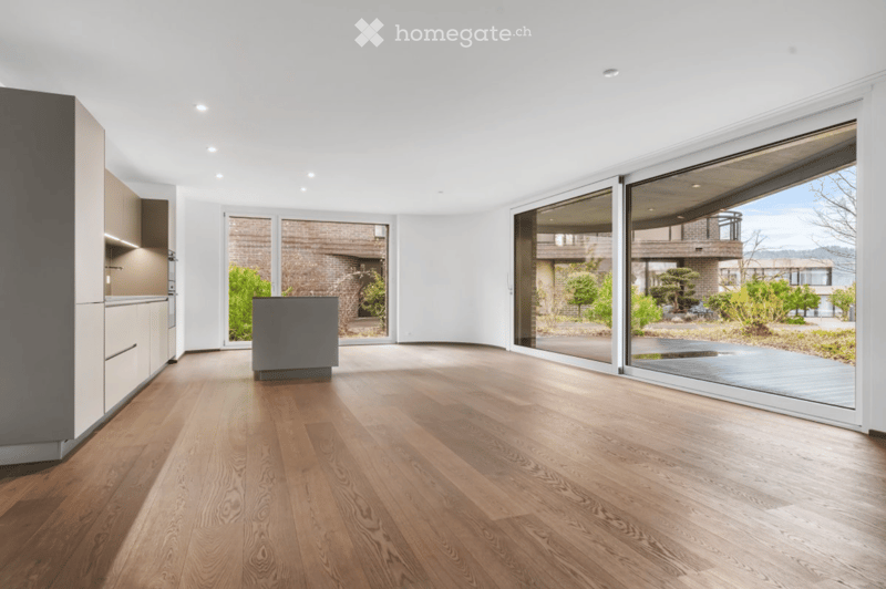 Bright, open-concept space with wooden flooring, large glass sliding doors, and a modern kitchen area visible on the left side.