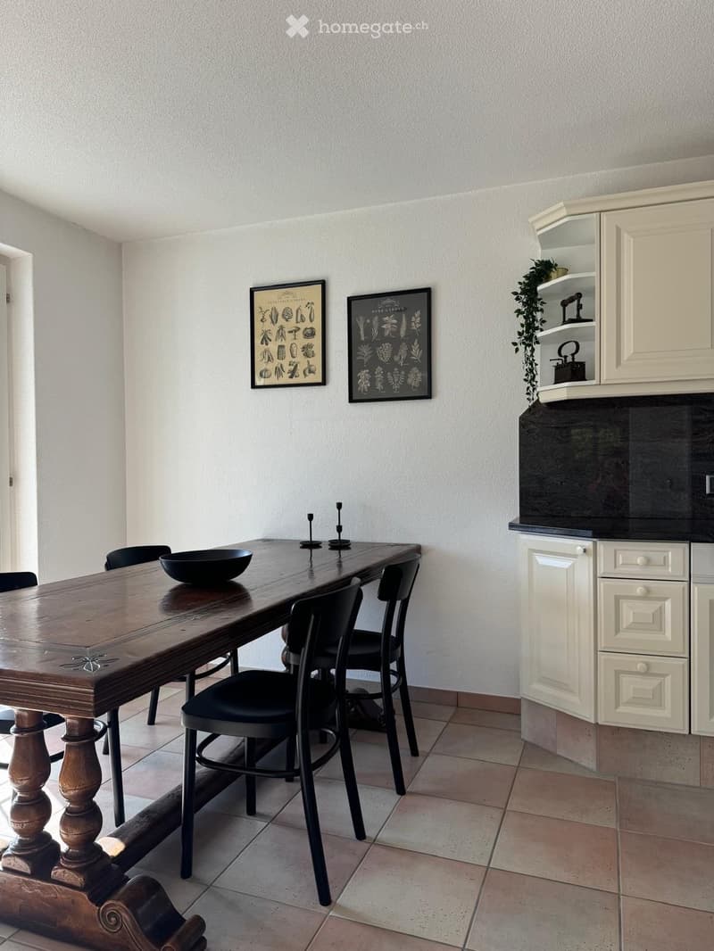 Dining area with a long wooden table, black chairs, a cabinet with glass doors, and decorative wall art.