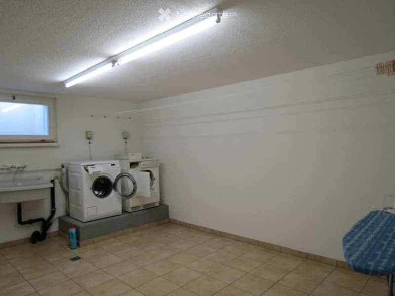 Laundry area with a washing machine, sink, and tiled floor.
