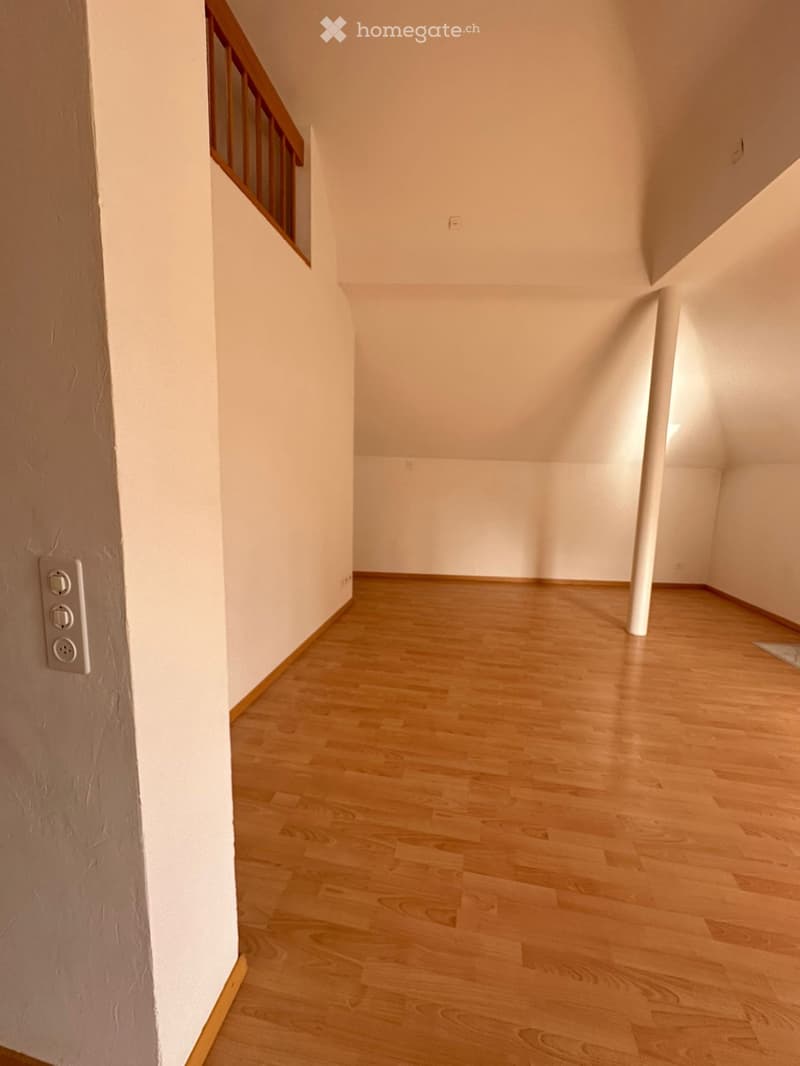 Empty hallway with wooden flooring, white walls, and a staircase with wooden railings visible on the left side.