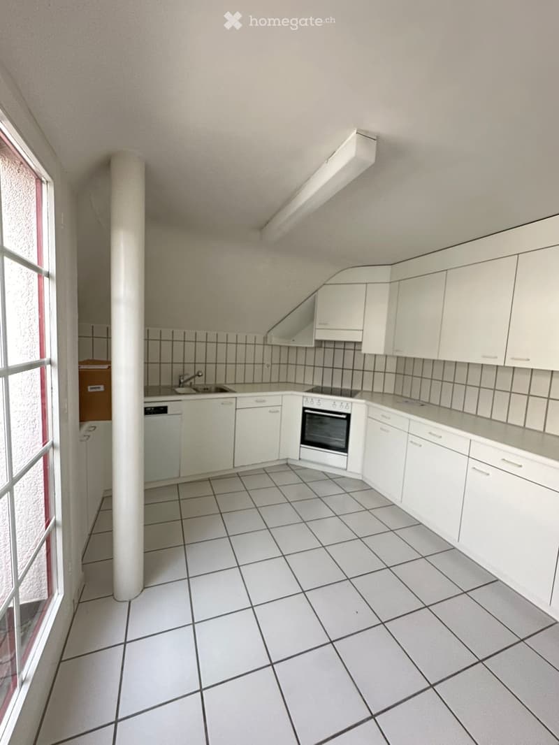 Empty kitchen with white tiled floor, white cabinets, sink, dishwasher, and oven. The walls have black and white tiled backsplash.