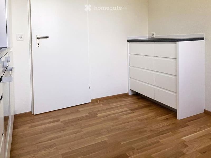 Empty room with light-colored walls, wooden flooring, and a white cabinet with drawers. No furniture or equipment is present.