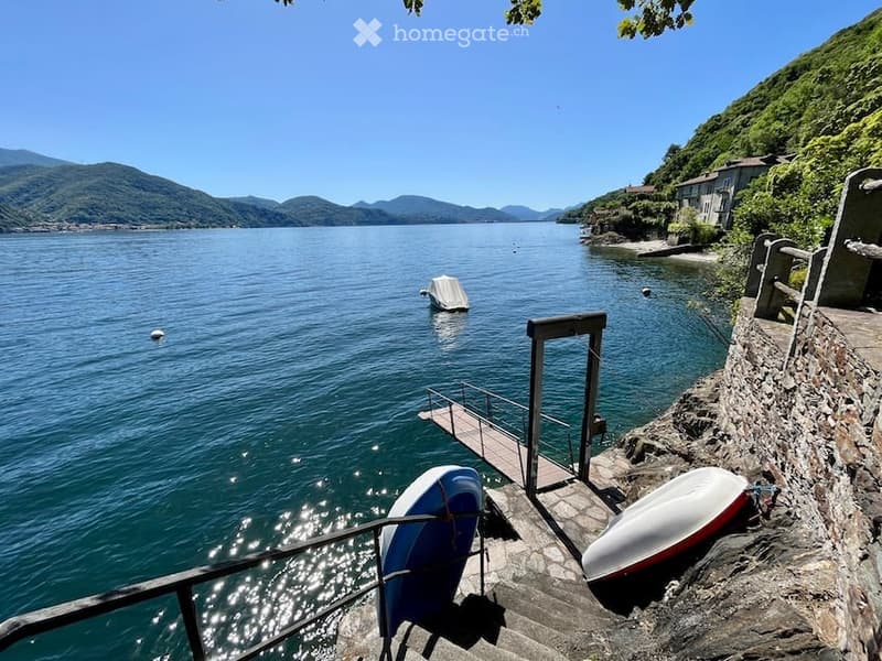 Lake shore with a dock and two boats, stone stairs, a mountain landscape