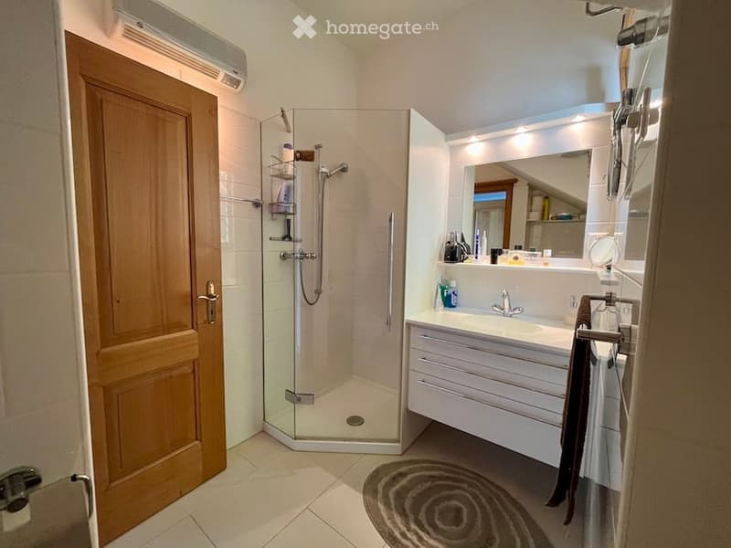Modern bathroom with a glass shower enclosure, a white vanity, a mirror, and a wooden door.