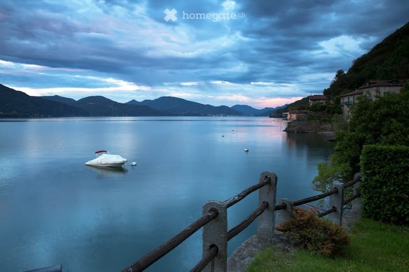 Calm lake with small boat, mountain landscape, wooden fence, greenery