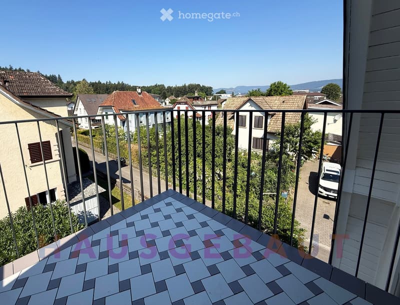 Balcony with tiled floor and metal railing, overlooking a residential neighborhood with houses, trees, and a parked car.