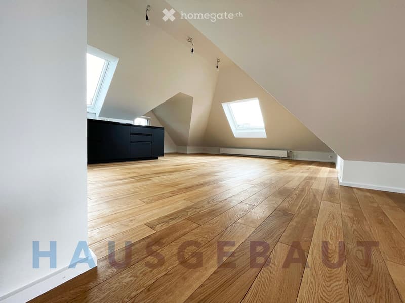 Empty attic room with wooden flooring, white walls, and skylight windows. No furniture or equipment present.