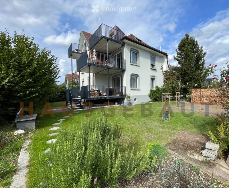Two-story house with white exterior, dark grey balcony, and well-maintained garden.