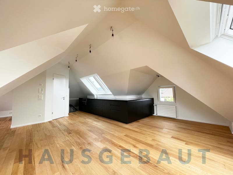 Bright, open attic space with wooden flooring, fitted kitchen cabinet, sink, and skylight windows.